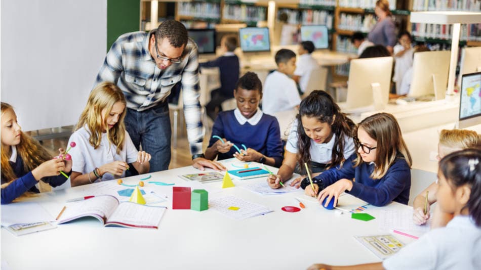 Método ABN para enseñar matemáticas; un profe habla con un grupo de alumnos de primaria con manipulativos