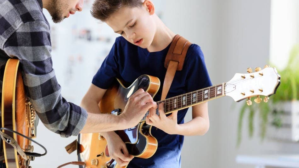 Profesor de conservatorio ayudando a un niño con una guitarra electrica