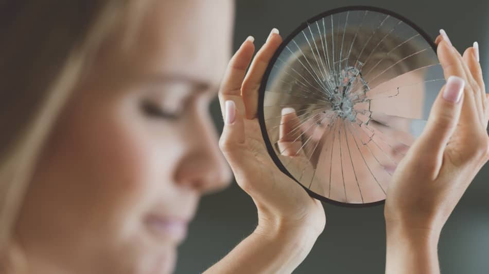 Síndrome del impostor, mujer reflejando su rostro en un espejo roto