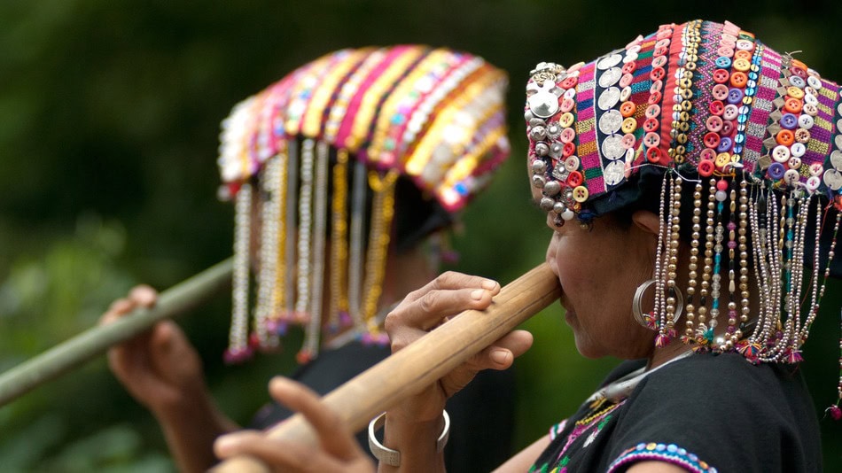 Etnomusicología, indígenas soplando un instrumento musical con la nariz