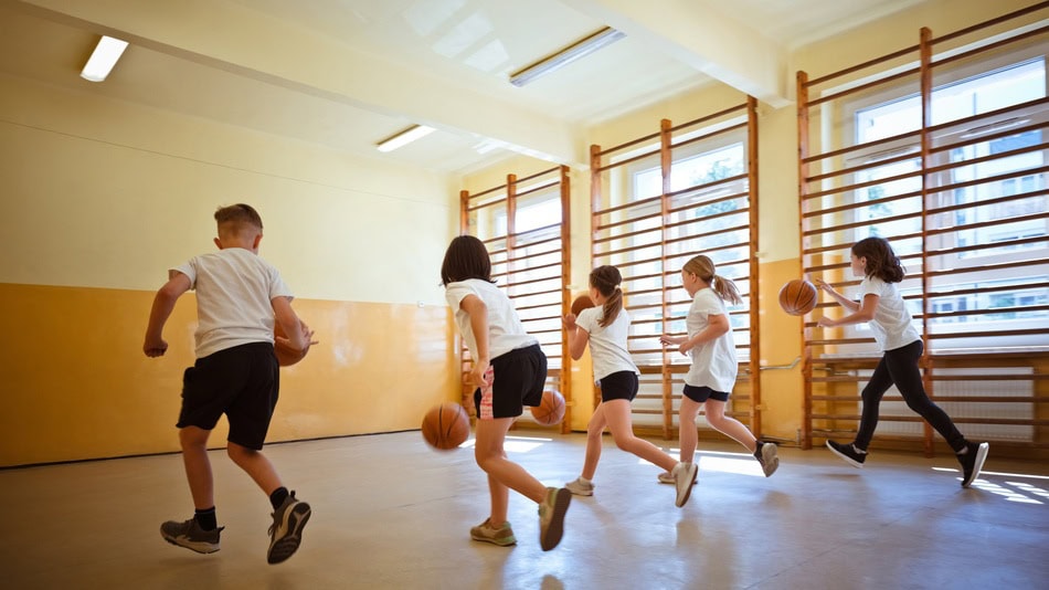 Niños en clase de educación física corriendo con balones