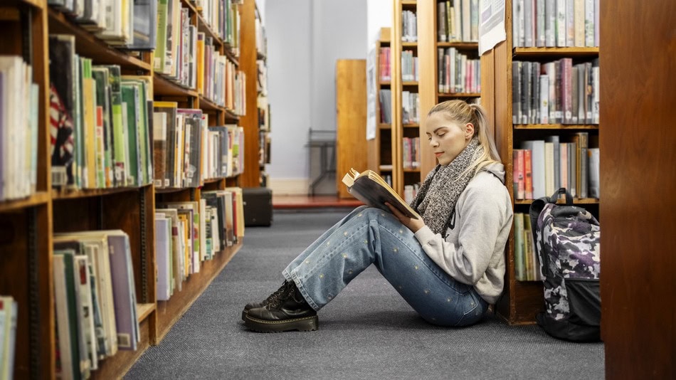 Alumna de bachillerato leyendo un libro sentada en el suelo de la biblioteca