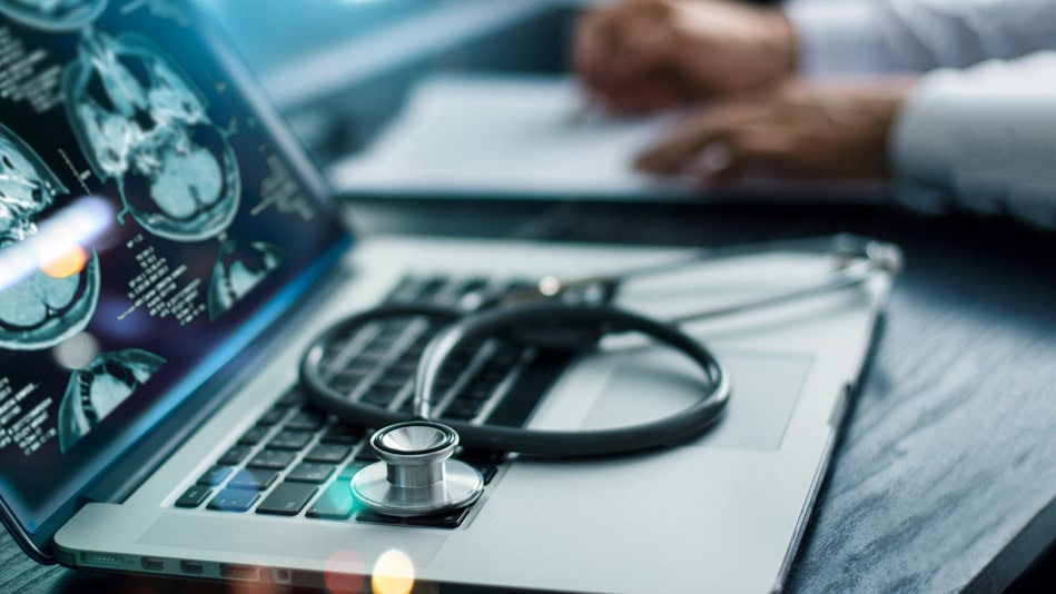 Neurólogo en su mesa de trabajo con un portátil abierto y un fonendoscopio