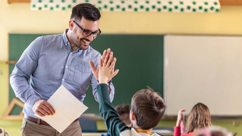 Educación, enseñanza inglés. Un profesor feliz choca la mano con un alumno.