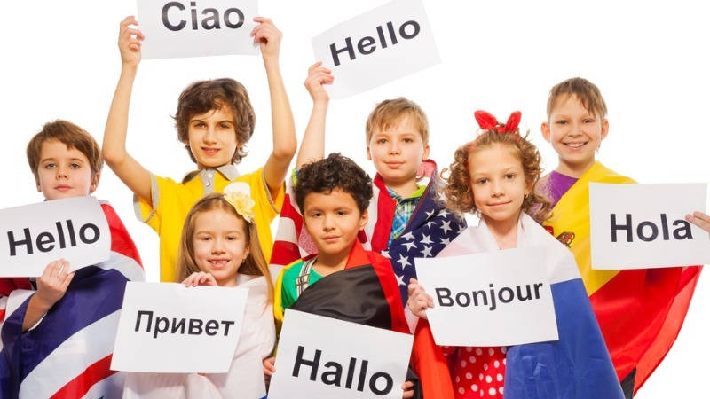 Educación multicultural. Un grupo de niños llevando banderas de distintos países y con carteles diciendo hola en varios idiomas.