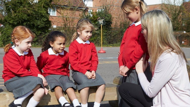 Educación, asertividad, resolución de conflictos. Una profesora habla con un grupo de niñas en el recreo.