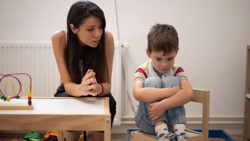 Educación, asertividad. Una profesora intentando explicar e animar a un niño en el aula.