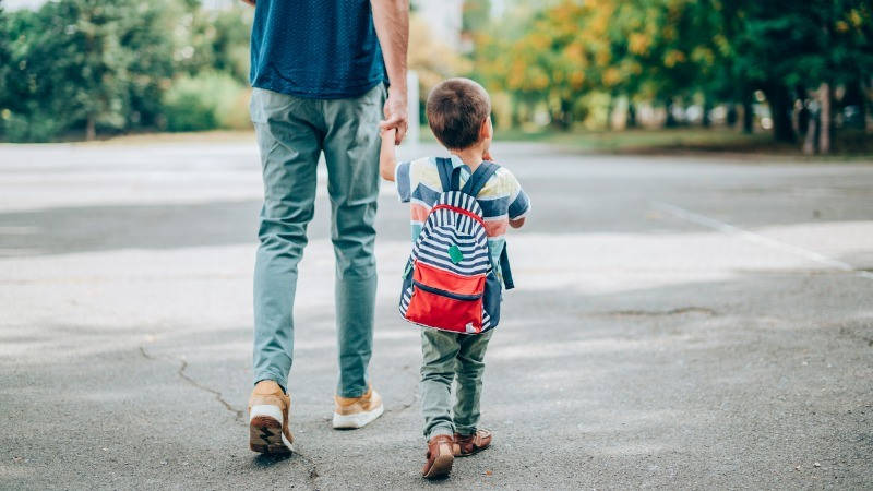 Educación, atención temprana; un niño con una mochila camina con su padre agarrados de la mano