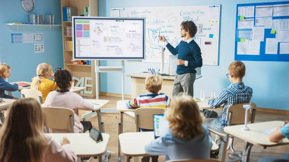 TIC en Educación Especial; un profe enseña con la pizarra digital y un niño le sigue con tablet o un mini ordenador