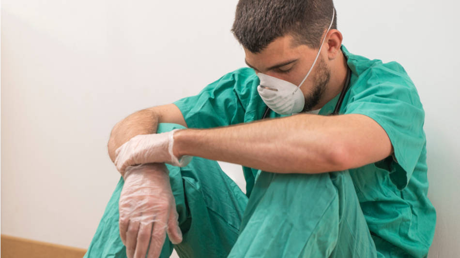 Enfermero cansado, triste, sentado en el pasillo del hospital con mascarilla y guantes