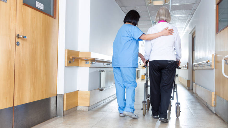 seguridad del paciente enfermería; una enfermera ayuda a una paciente mayor pasear por los pasillos del hospital