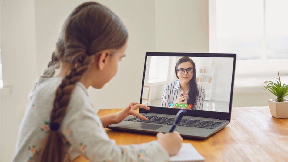 Niña en clase online con la profe en la pantalla del portátil 